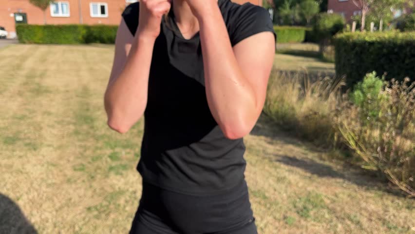 Front view of a fit young woman exercising outdoors in the sun, shadow boxing
