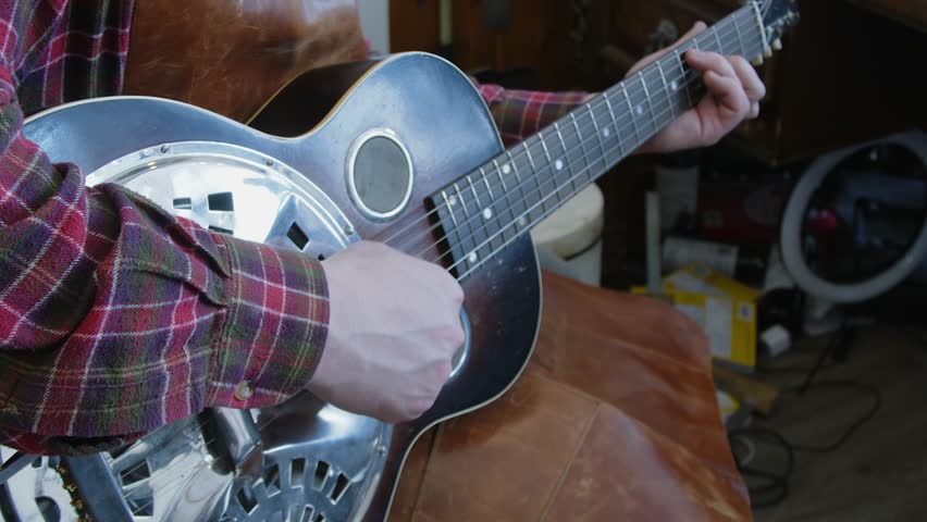 Guitar tech in leather apron plays National Steel guitar in work shop