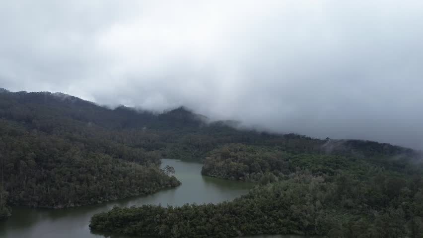 A peaceful mountain lake surrounded by dense forest and scenic hills, capturing the calm natural beauty of a pristine wilderness landscape with reflections on the water surface.