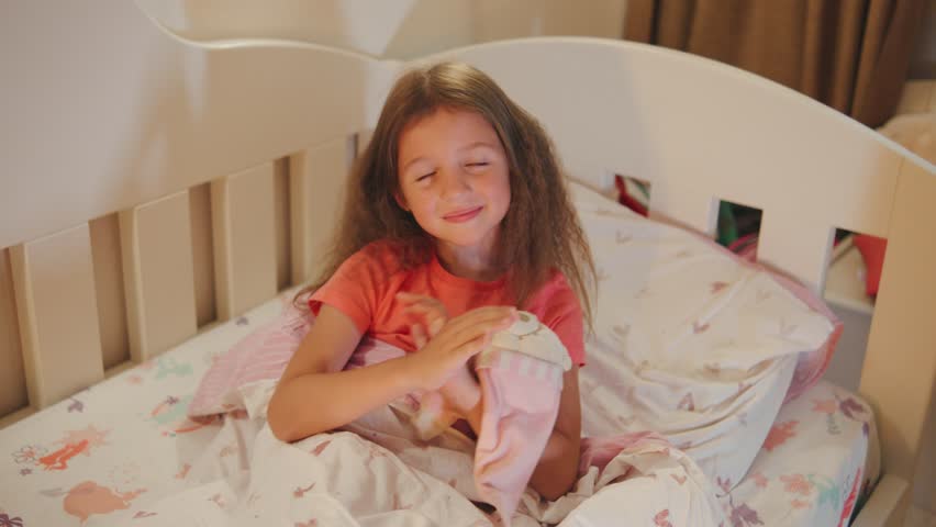 Young girl sleeps soundly in bed during morning hours in a cozy bedroom filled with toys and colorful sheets