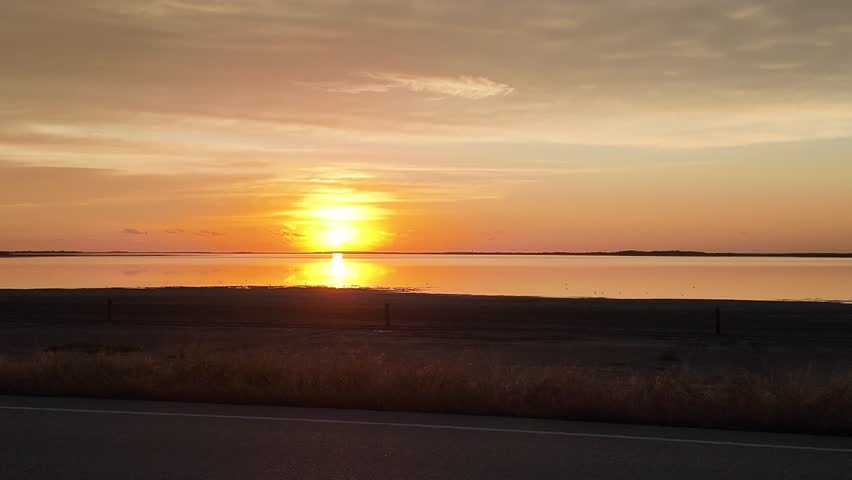 Golden sunrise over calm water with bright reflection on the surface. Scenic nature landscape at dawn with slow panning camera movement