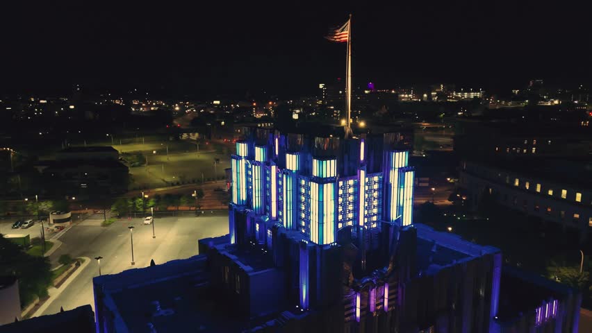 Aerially circling the illuminated crown of an iconic building as the American flag flutters through the night.