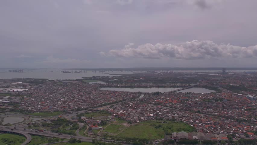 A wide aerial shot of Surabaya, Indonesia, highlighting the contrast between coastal seaport areas, urban water management reservoirs, and the vast expanse of residential neighborhoods
