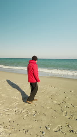an elderly man throws stones into the sea wearing a red jacket