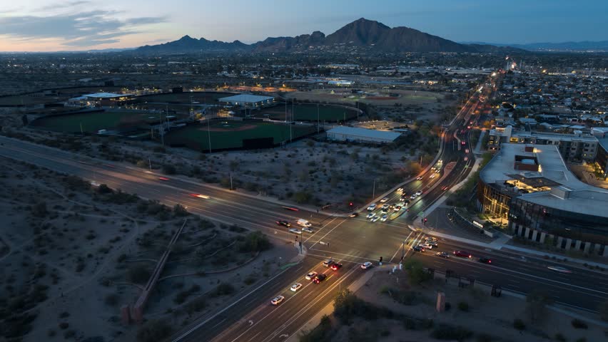 Timelapse drone shot of a sunset intersection with Camelback Mountain in Scottsdale, Arizona in the background with mountains and desert landscape.