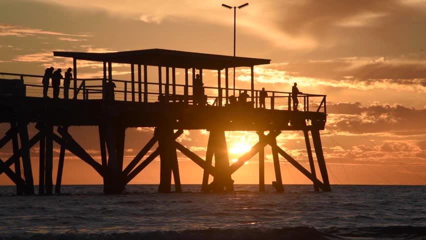 Silhouettes of people enjoying a beautiful sunset and fishing from the jetty with golden light reflecting on the sea
