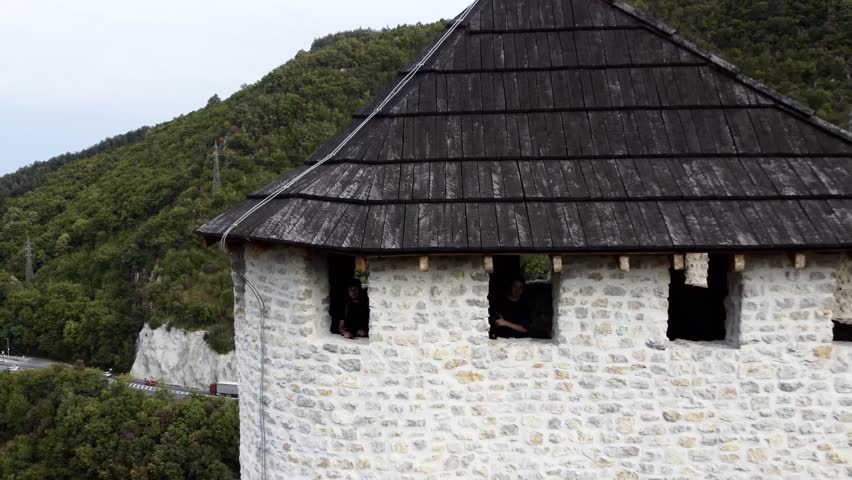 Medieval cliff-top fortress overlooking river and red-roofed town in Uzice, Serbia, with winding road. g.