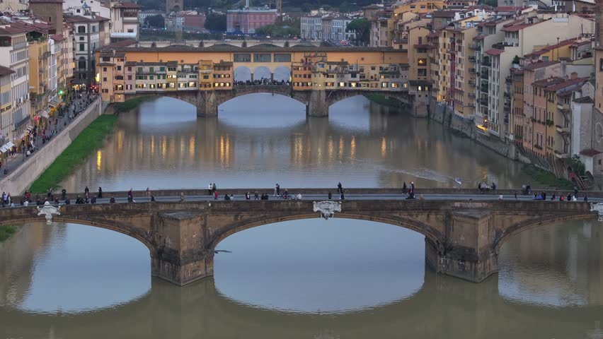 Timelapse push in shot over the Arno River at twilight revealing the historic Ponte Vecchio bridge with city lights in Florence, Italy.