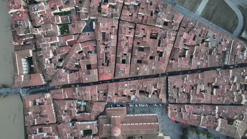 Top-down drone shot gliding over dense terracotta roofs to reveal the majestic Palazzo Pitti in Florence, Italy, under soft overcast light.