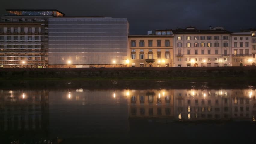 Cinematic pan shot across illuminated historic buildings reflecting on the Arno River in Florence, Italy, at night, 4K aerial footage.