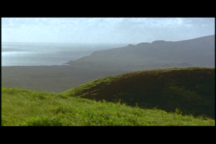 Camera pans left across rolling green hills of Easter Island, Chile.