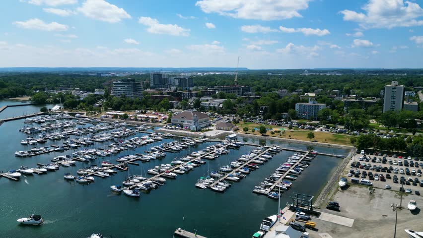 Drone view of Bronte Harbour marina filled with docked boats and yachts near waterfront park and urban skyline on sunny summer day along Lake Ontario shoreline. Oakville, Ontario. June, 12, 2025
