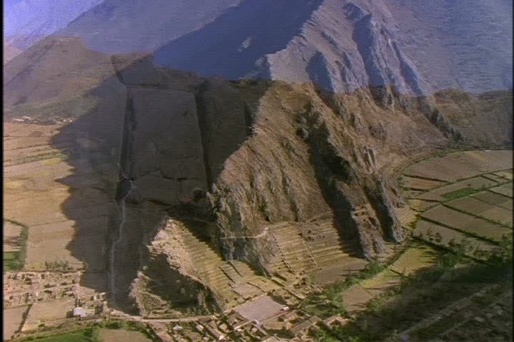Aerial shot over green peaks of the Andes Mountains in Peru, camera zooms in to ruins of Machu Picchu.