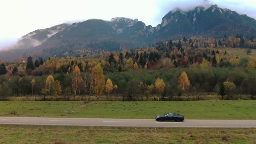Establishing aerial rolling shot of luxury coupe sport car driving on a mountain road. Car driving fast on the road 
