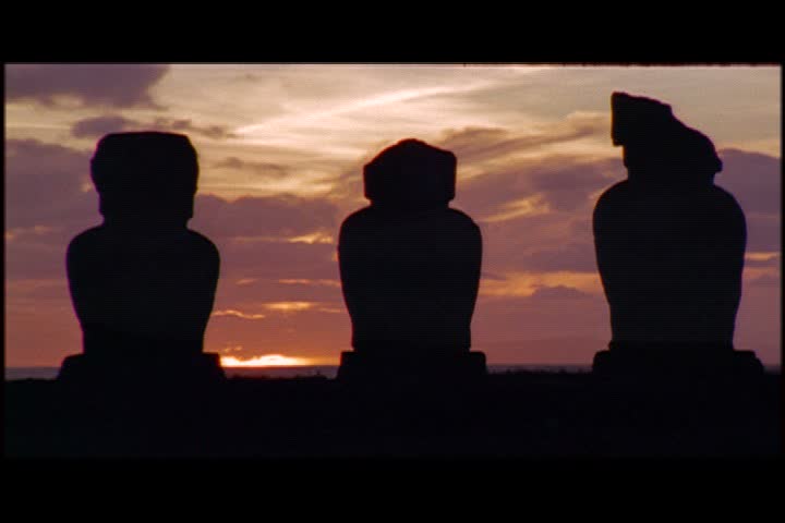 MS silhouettes of three moai statues against pink and purple clouds at sunset on Easter Island, Chile.