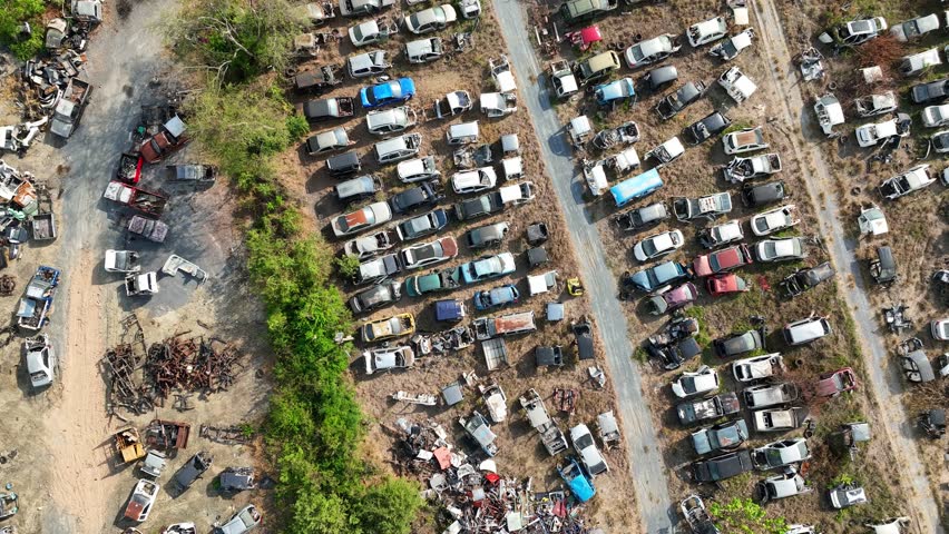 Aerial drone view of a car scrapyard filled with hundreds of abandoned vehicles arranged along dusty lanes, illustrating automotive recycling, scrap metal recovery, and end-of-life vehicle management.
