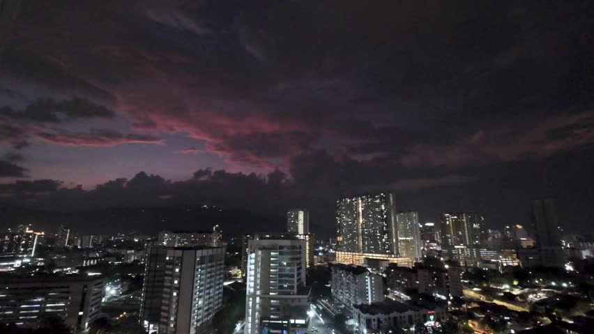 Breathtaking high-angle view of George Town, the vibrant capital of Penang Island in Malaysia, captured at sunset. The modern high-rise buildings glow with warm lights as dramatic pink, purple, and orange clouds fill the evening sky. Lush hills rise in the background, adding depth to this stunning urban panorama. The scene transitions from golden dusk to illuminated night, showcasing the perfect blend of modern architecture and natural beauty in Southeast Asia. Ideal stock video footage for travel documentaries, city promotions, atmospheric backgrounds, tourism projects, or Asian destination visuals. High-quality, royalty-free clip perfect for commercials, websites, and creative edits.

