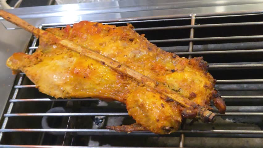 Traditional Thai grilled chicken (Gai Yang) skewered on a bamboo stick and roasting on a metal electric grill.