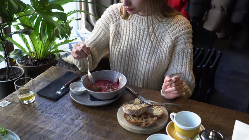 young beautiful woman eats borscht with spoon in cafe, girl eats soup with lard and bread in restaurant