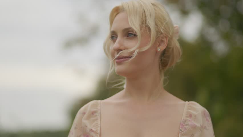A blonde woman in her middle age, smiling confidently while enjoying the fresh air and bright outdoor environment.