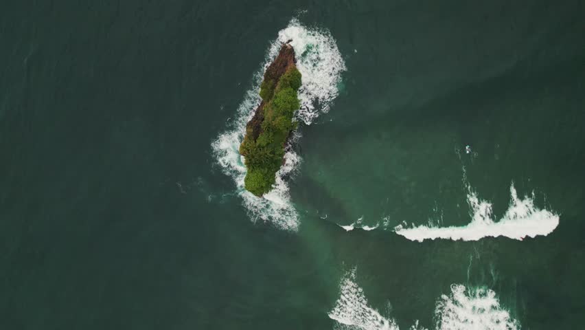 Vertical Top-Down Aerial Shot of Waves Crashing Against a Small Rocky Island