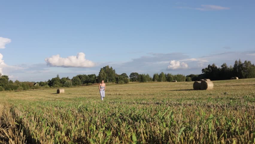 A woman in sportswear walks through a field in a village on a sunny summer day