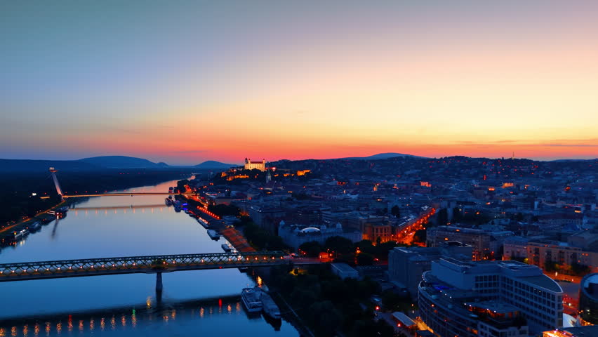 Old City is switching on lights at dusk time. Drone footage over the Danube River near the Old Bridge in Bratislava, Slovakia.