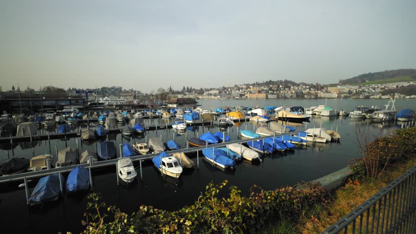 Several boats moored at the harbor of Lake Lucerne with the city architecture in the background.