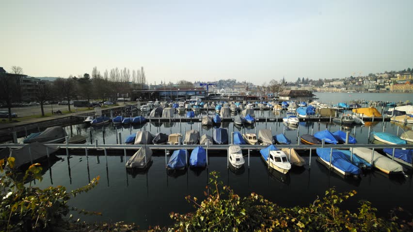 Several boats moored at the harbor of Lake Lucerne with the city architecture in the background.