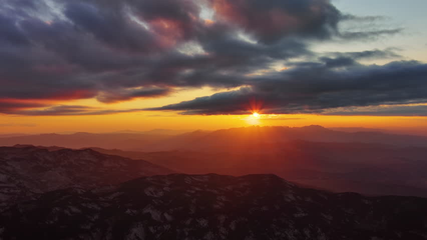 Orange sun setting over mountain with dramatic clouds. Beautiful evening sky at sunset with orange light, aerial view 4k