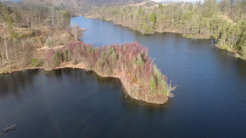 Aerial drone view of peaceful forest lake surrounded by trees and hills in the UK