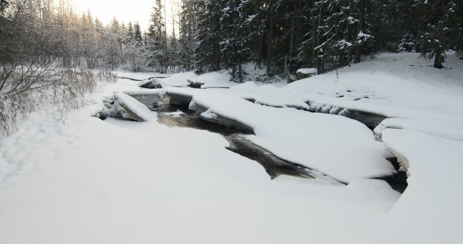 Tranquil, partially frozen river flowing through a snow-covered forest during winter, Matarinkoski, Vantaa, Finland, Europe.