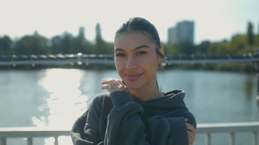 A radiant teenage girl gazes into the camera with a wide smile, her brunette hair blowing gently in the breeze, as she enjoys a carefree afternoon in the park.