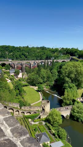 Luxembourg - May 30 2023: Panoramic view of Luxembourg capital. Overlooking Luxembourg City, the image showcases the historic church with a tall, pointed spire as a prominent feature. Surrounded by classical European architecture with grey roofs, the scene includes lush greenery and a calm river in the foreground. The layout demonstrates Luxembourg