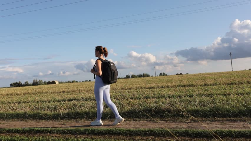 A woman in sportswear walks through a field in a village on a sunny summer day