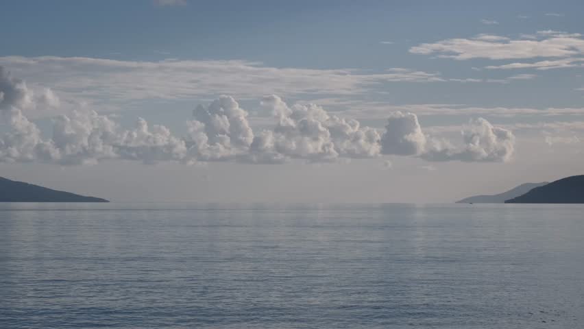 Fluffy white clouds moving in straight line slowly above the Adriatic Sea near Opatija, Croatia. Real time magnificent nature background with calm summer atmosphere.