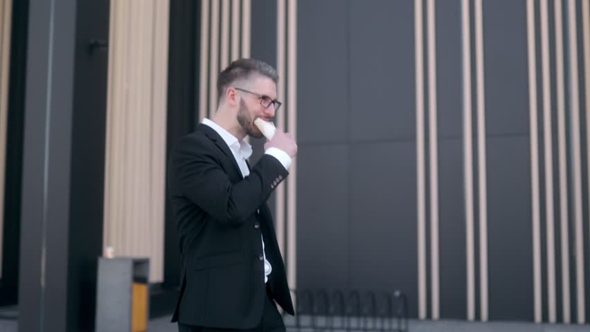 Manager in a suit happily savoring a sandwich in a busy urban center surrounded by tall buildings.