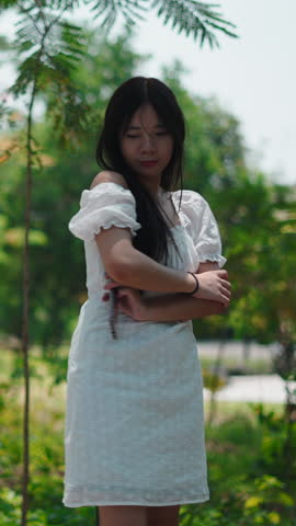 Young woman in white dress posing and dancing in a green summer park on a sunny day