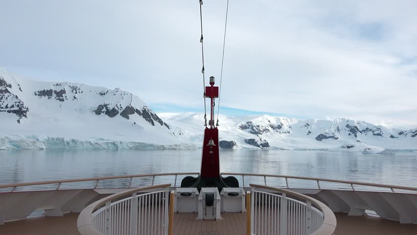 A ship navigates icy waters in Antarctica, with stunning views of snow-covered mountains and ice formations. The time is around noon, giving a clear look at the landscape.