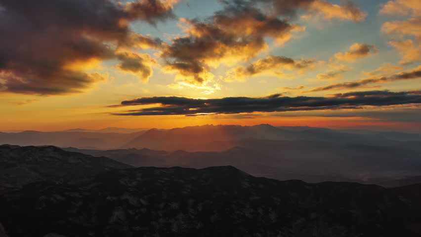 Orange sun setting over mountain with dramatic clouds. Beautiful evening sky at sunset with orange light, aerial view 4k