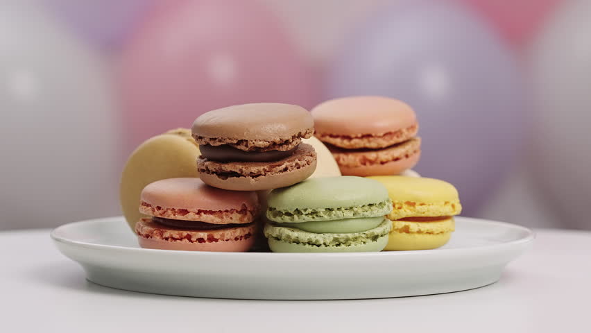 Set sweet French macarons turning plate. Vibrant balloons decorations background. Family celebration anniversary party dessert table. Delicious confectionery pastry gift concept professional stock 