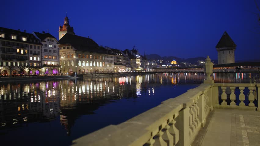 Night shot of the city of Lucerne at night with glowing lights reflecting in the water of Lake Lucerne and the Reuss river.