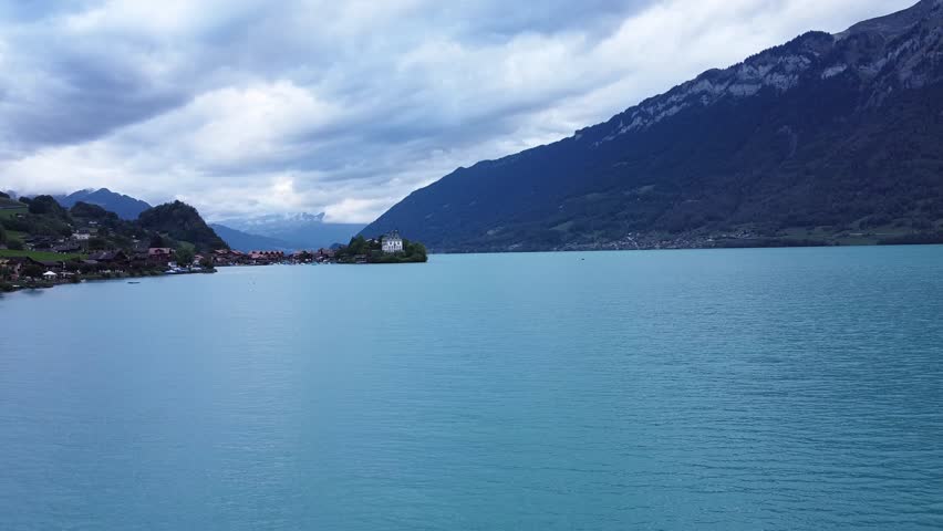 Mountain lake with turquoise water, small village and castle on shoreline under dramatic cloudy sky
