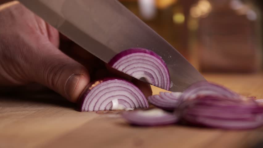A chef cuts onions for a salad on a cutting board. Close-up.