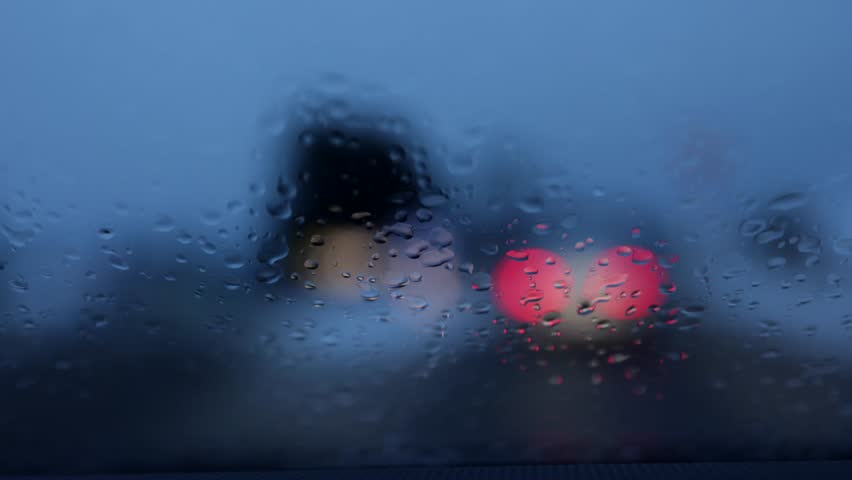 Cars moving in rain seen through wet windshield. Headlights traffic bokeh scene.