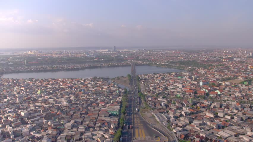 Dense urban housing and infrastructure in East Java: A wide-angle panorama showing the intricate grid of residential rooftops, a major roadway bridge, and the coastal landscape of Surabaya, Indonesia