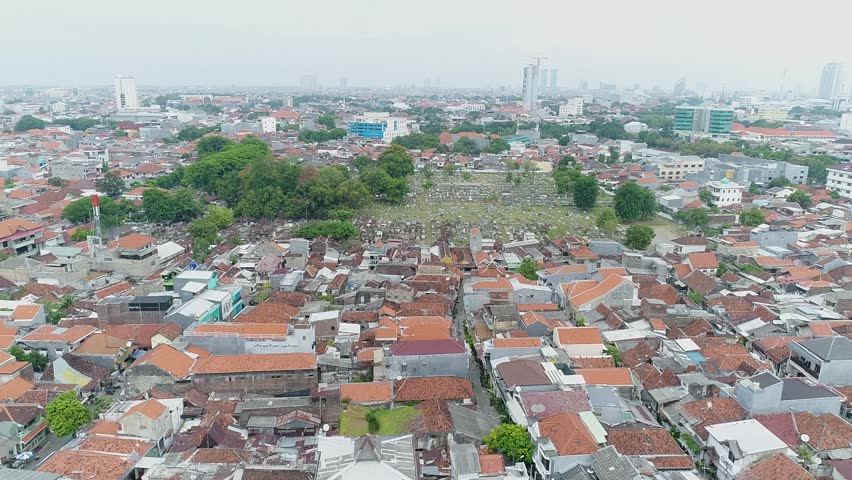 High-angle aerial view of a crowded public cemetery nestled in the heart of a dense urban residential area in Surabaya, Indonesia