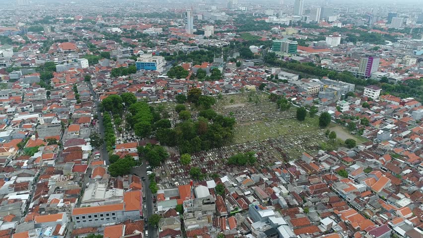 A sprawling historical graveyard, known as Kampung Seribu Makam, integrated into a vibrant urban neighborhood in Surabaya, showcasing the intersection of life and history