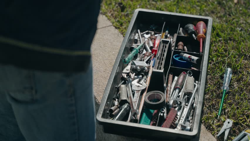 Open toolbox filled with assorted hand tools placed on ground outdoors