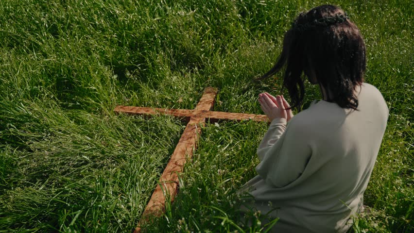 Jesus kneeling in grass holding wooden cross representing crucifixion and Easter passion